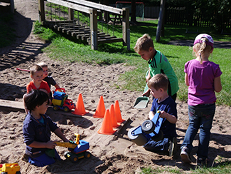 Sechs Kinder spielen im Sand mit Bagger und Co.